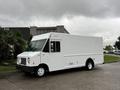 A white 2011 Ford Econoline delivery truck with a boxy design and large side door parked on a roadway