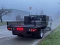 A 2015 Ford F-550 truck with a flatbed, equipped with a metal mesh railing and various attachments in the cargo area, shown from the rear perspective