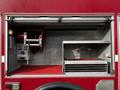 Interior compartment of a red 1994 Freightliner FL80 featuring a hose reel and storage shelves with a gauge and valve visible