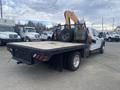 A 2017 Ford F-550 flatbed truck with a mounted backhoe attachment on the rear and a rugged black bed with round tail lights