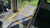 A yellow wheelchair ramp extended from the entrance of a bus with textured flooring and metal grab rails on either side