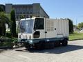 A 2001 Tennant 830-II street sweeper vehicle with a compact design featuring a white and teal exterior and front-mounted brushes for cleaning streets