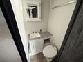 Interior view of a bathroom featuring a white sink with two faucets a mirrored cabinet and a toilet against plain walls