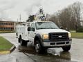 A white 2006 Ford F-450 utility truck with a ladder and work equipment mounted on the back parked on a wet surface