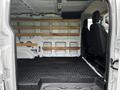 A 2023 Ford Transit van interior featuring wooden shelves along the back and two front seats without any cargo or additional items visible