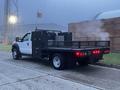 A 2015 Ford F-550 with a flatbed and a black metal frame visible in the foreground emitting steam from the rear with a flag mounted on the cab