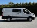 A 2023 Ford Transit in white, featuring a high roof, sliding side door, and large wheels, positioned in profile view with a sleek, modern design