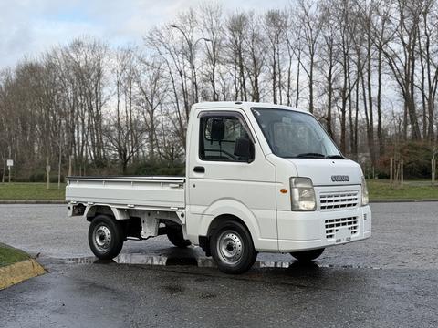 A white 2009 Suzuki Carry truck with a flatbed and compact design parked on a paved surface