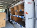 Interior of a 2012 GMC Savana van featuring wooden shelving units secured with blue straps against a white metal wall