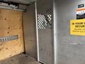 A 2022 GMC Savana interior with a metal partition featuring circular cutouts and a wooden wall on one side, along with a warning sign about security and a storage slot on the other side