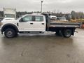 A white 2021 Ford F-550 truck with a flatbed and black fenders parked on a wet surface