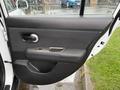 The interior side door panel of a 2012 Nissan Versa featuring a black handle and armrest along with control buttons in a minimalist design