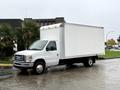 A white 2013 Ford Econoline box truck parked on a wet surface with a plain cargo area and a single cab design