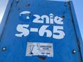 A blue lift labeled Genie S-65 with visible wear and a caution sign indicating electrocution hazard