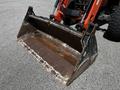 A rusted metal bucket attachment for a 2011 Kubota M8540D tractor with an angled front and reinforced edges