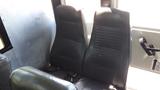 Two black vinyl seats with vertical stitching and seatbelts in a bus interior