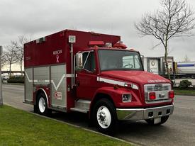 A red 1995 Freightliner FL70 rescue vehicle with a silver stripe and emergency lights on top parked on the street