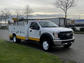 A 2019 Ford F-550 truck with a white cab and yellow accents featuring a service body with storage compartments on the sides