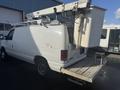 A white 2008 Ford Econoline van equipped with a bucket lift mounted on the roof and a flatbed rear for access and utility work