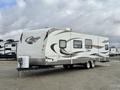 A 2013 Keystone Cougar travel trailer with a streamlined design featuring a white exterior and gray accents, parked with a hitch at the front