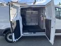 A 2016 Ford Transit van with its doors open revealing the interior space equipped with shelving and a fire extinguisher mounted on the wall