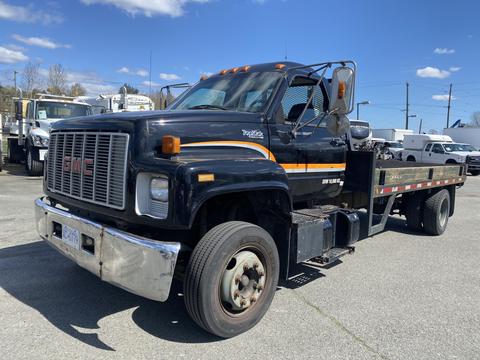 A black and orange 1996 GMC Top Kick flatbed truck facing slightly to the right with a large, chrome front bumper and a visible ladder on the side