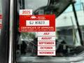 A red and white certificate of approval sticker with the text "CERTIFICATE OF APPROVAL" and various months listed, attached to the window of a vehicle