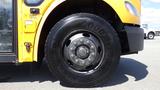 A yellow 2014 Freightliner Thomas diesel school bus with a large black tire and a visible chrome wheel hub