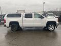 A white 2015 GMC Sierra 1500 truck with a shell on the bed and a crew cab design parked on a wet surface