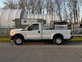 A white 2012 Ford F-250 truck with a flatbed parked in profile view