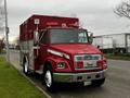 A red 1995 Freightliner FL70 fire rescue truck with various lights on the roof and silver details parked on a street