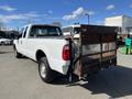 A white 2013 Ford F-250 SD pickup truck with a flatbed and a metal gate at the back parked on a lot