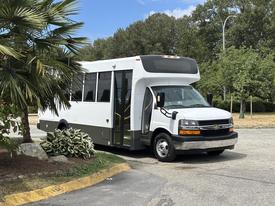 A 2020 Chevrolet Express bus painted white with black accents features large windows and a sliding door on the side