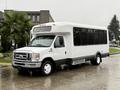 A white 2014 Ford E-450 shuttle bus with large windows and a sliding door parked on a wet surface