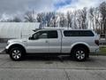 A white 2014 Ford F-150 with a crew cab and a cap on the truck bed displayed in profile view