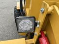 A close-up of a square LED work light mounted on a yellow frame with visible electrical connections and a hydraulic component