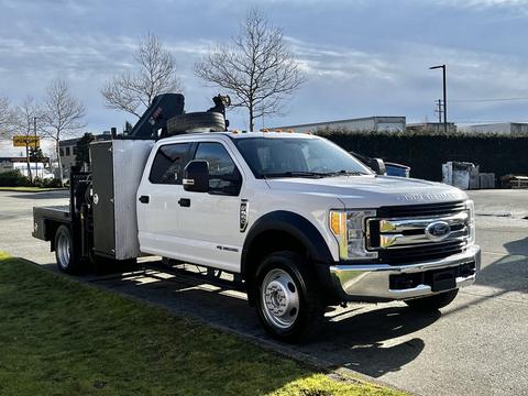 A white 2017 Ford F-550 truck with a flatbed and tool box attached is parked on a lot