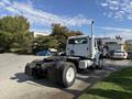 A white 2003 Freightliner M2 106 truck with a flatbed design and large rear tires is parked, showing its cab and exhaust stack