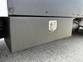 A silver and black storage box mounted on the side of a 2010 Peterbilt 320 truck with a latch mechanism visible