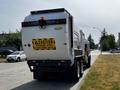 A 2010 Peterbilt 320 garbage truck with a white and black exterior featuring a caution sign indicating frequent stops and a right-hand drive notice