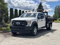 A white 2017 Ford F-550 with a flatbed and safety lights on top parked on a road