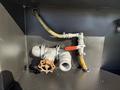 Close-up of piping and valves connected to a 2014 Hino 195 featuring a bronze valve a yellow hose and a gray pipe fitting