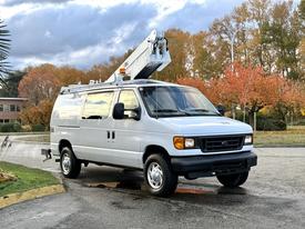 A 2007 Ford Econoline van with a raised utility ladder on top parked on a road