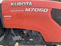 The image shows a red 2014 Kubota M7060 tractor featuring the logo and model number with visible mechanical components on the side