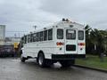 A 2016 International CE300 school bus with a white body and multiple lights on the roof, featuring large windows and a rear emergency exit door
