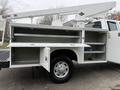A white 2001 Ford F-350 utility truck with an open service body showing multiple compartments and a lift mechanism on top