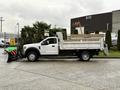 A white 2021 Ford F600 flatbed truck with a snowplow attachment on the front and wooden sides on the bed