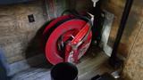 A red hose reel mounted on a wooden surface with a black hose coiled around it