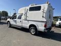 A white 2014 Ford F-350 SD with a custom truck camper shell featuring side access doors and a roof-mounted air conditioning unit