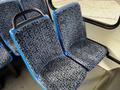 A pair of blue and black patterned bus seats with a black grab handle on the left seat